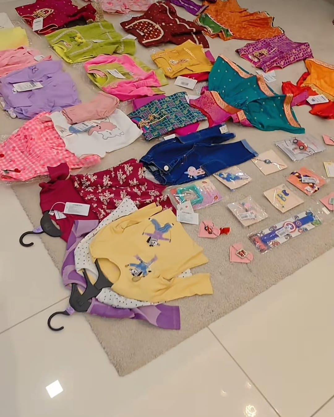 Kids outfits, hair accessories and small toys spread across a rug during a home try-on session