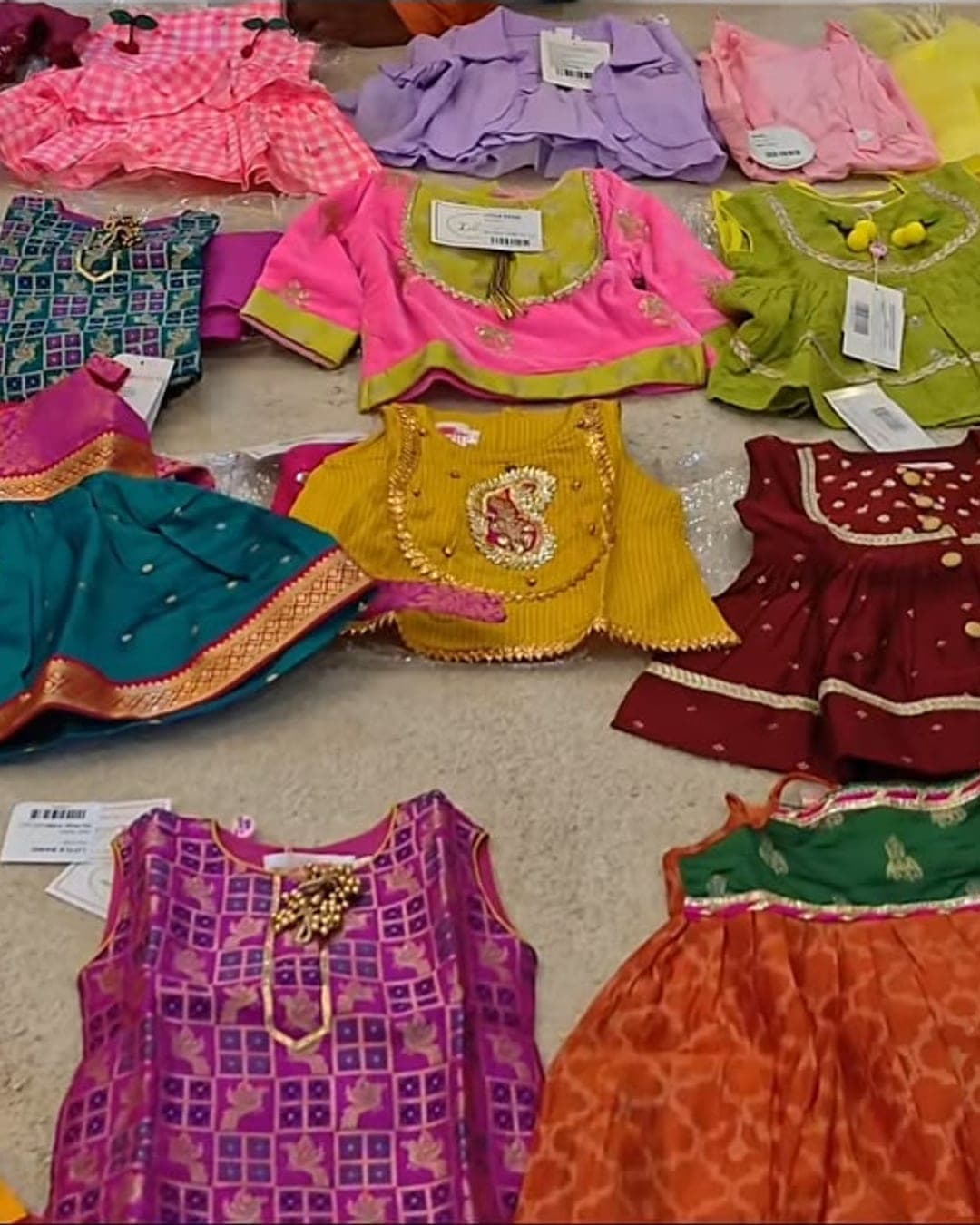 A close-up of brightly coloured kids ethnic outfits with tags still on, laid out on the floor