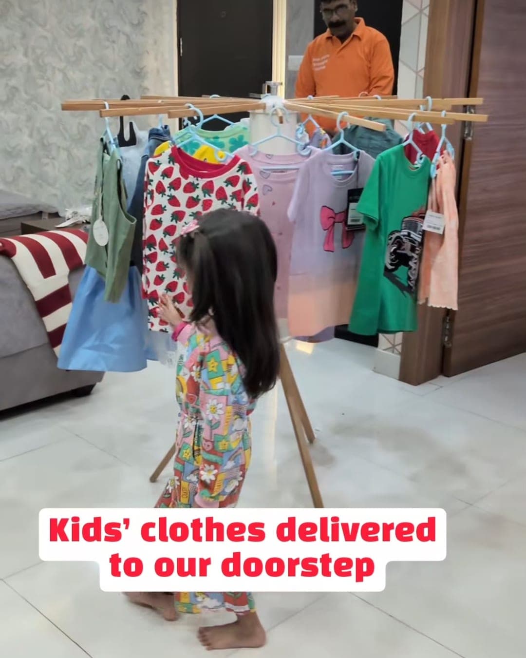 A toddler walking towards a rail of dresses set up inside her home, with a Skipzy stylist standing behind it
